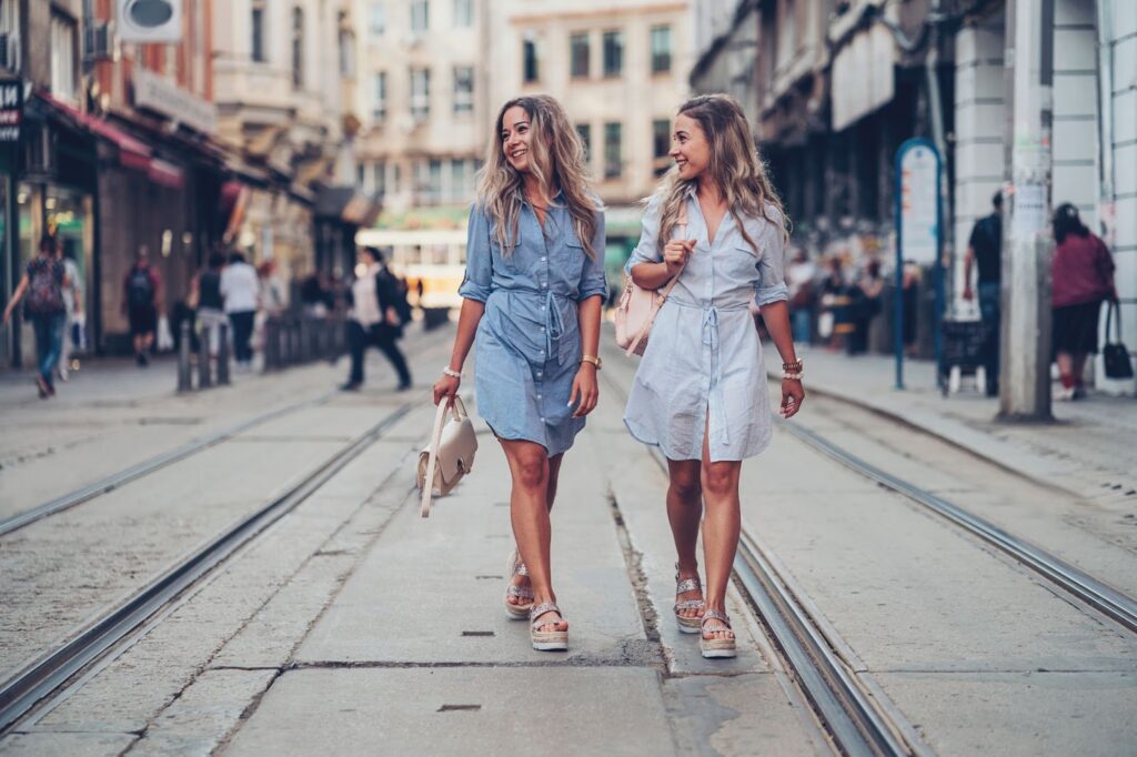 Dvi gatve einančios moterys, apsivilkusios džinsinėmis suknelėmis ir avinčios basutes su platforma