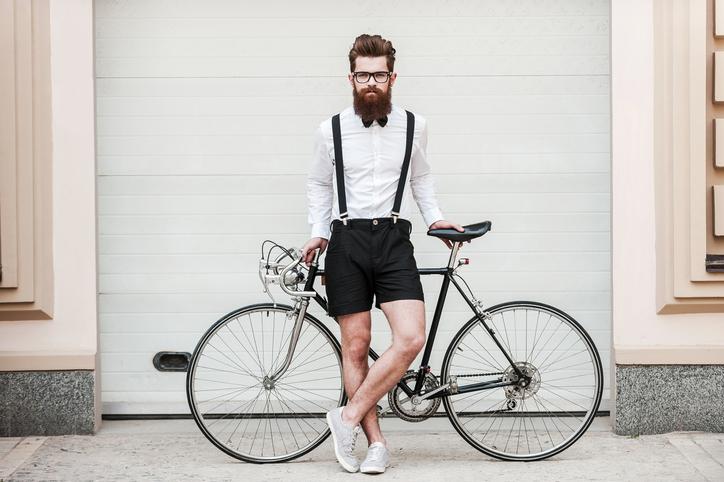 Hipsteris, dėvintis baltus marškiniu ir juodus šortus, stovi prie dviračio