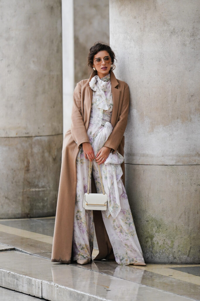 Moteris, dėvinti gėlėtą kombinezoną, ilgą paltą ir aukštakulnius batelius