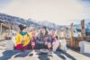 Keturi žmonės, dėvintys slidinėjimo drabužius, gurkšnoja gerimus kalnuose