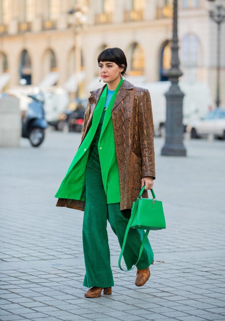 Moteris, dėvinti žalius drabužius, rudą paltą ir rudus aulinukus