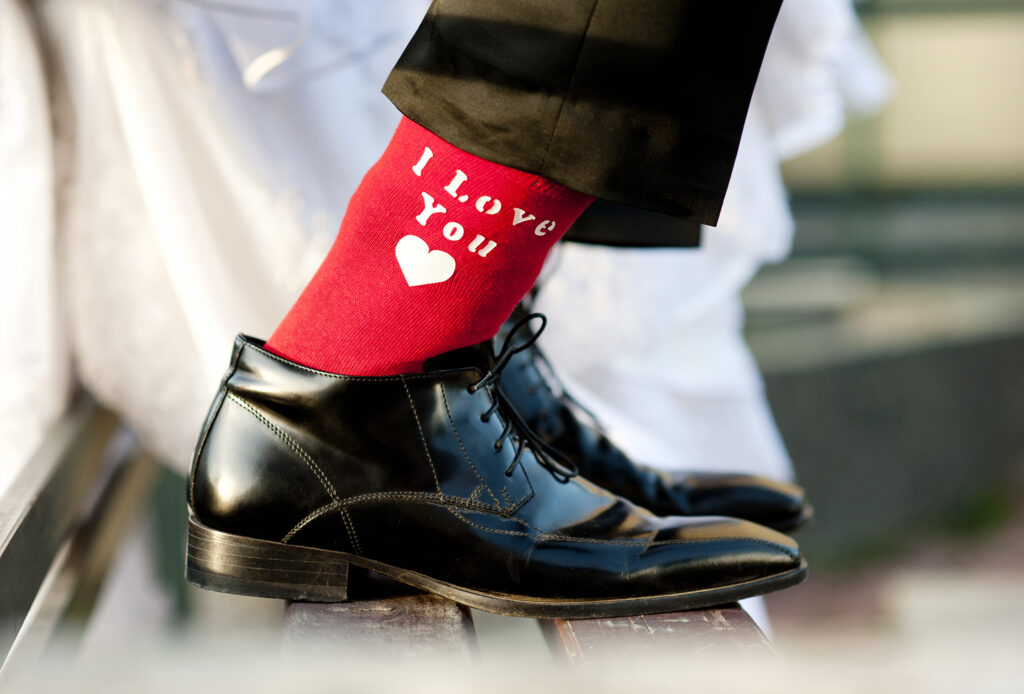 Vyras, avintis juodus vestuvinius batus ir mūvintis raudonas kojines su užrašu “I love you”